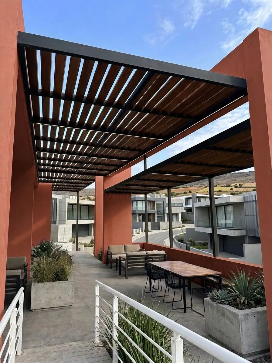Pérgola instalada sobre una terraza con muros color terracota y vista a un fraccionamiento.